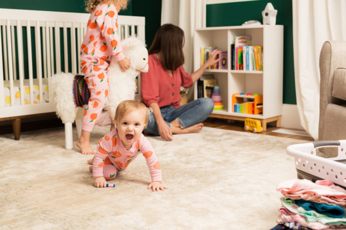Child crawling on nursery floor, mother and sister in background