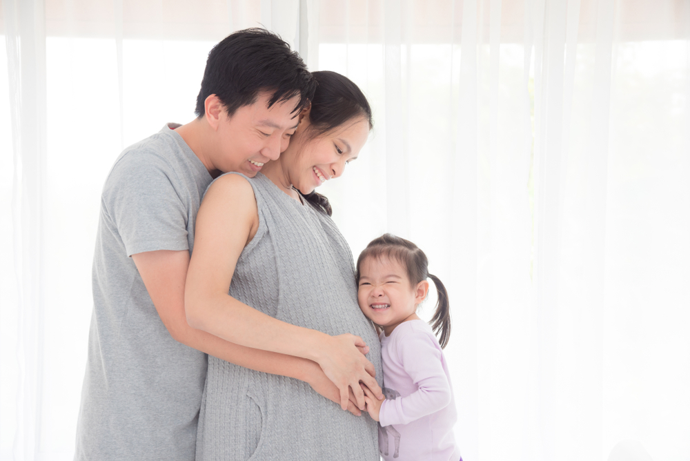 Asian man and his daughter hugging pregnant wife and smile together