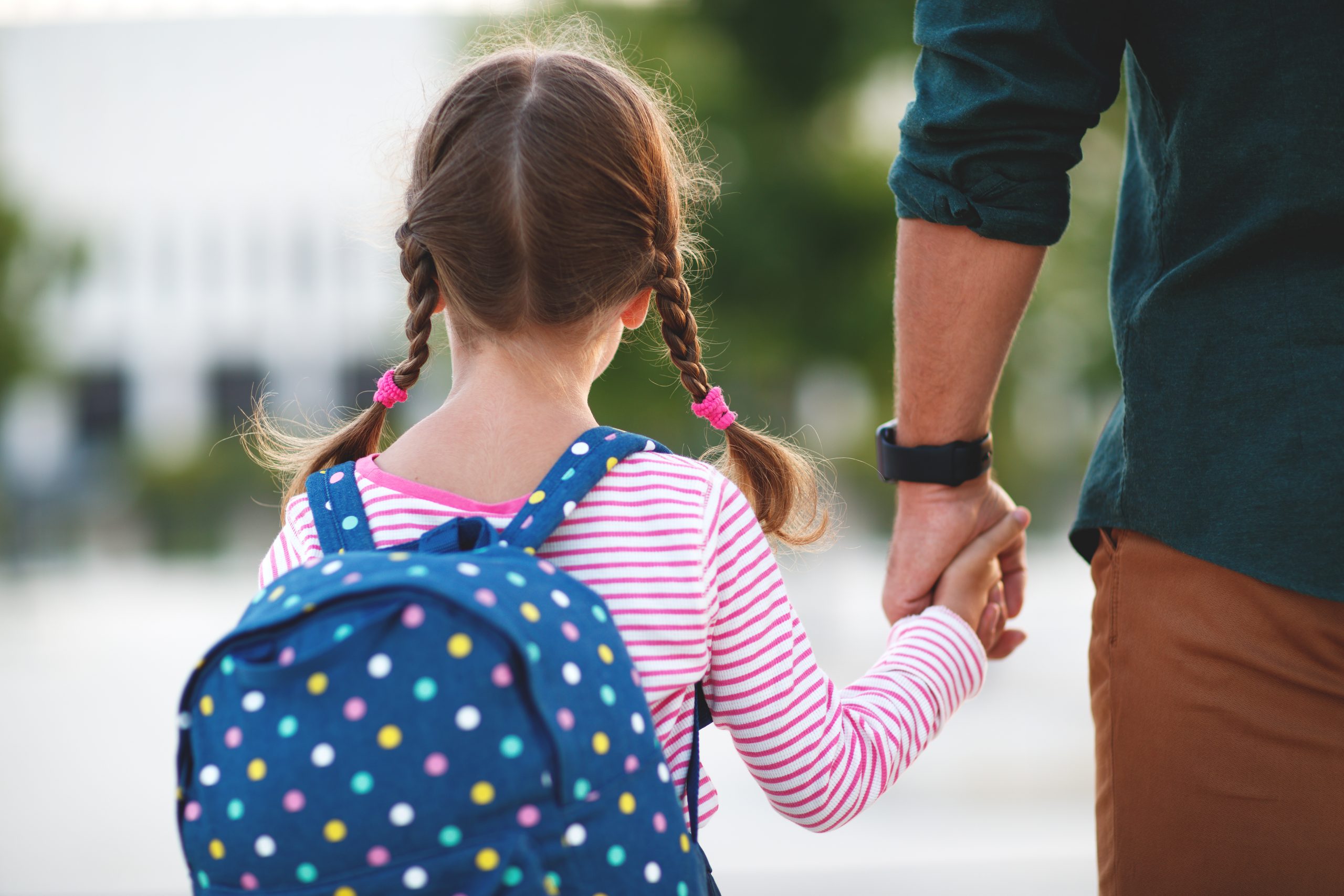 Back of girl with backpack on, holding hands with adult