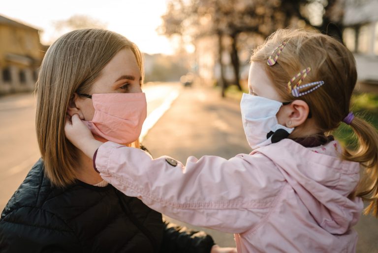 Little girl and mother facing each other both wearing masks.