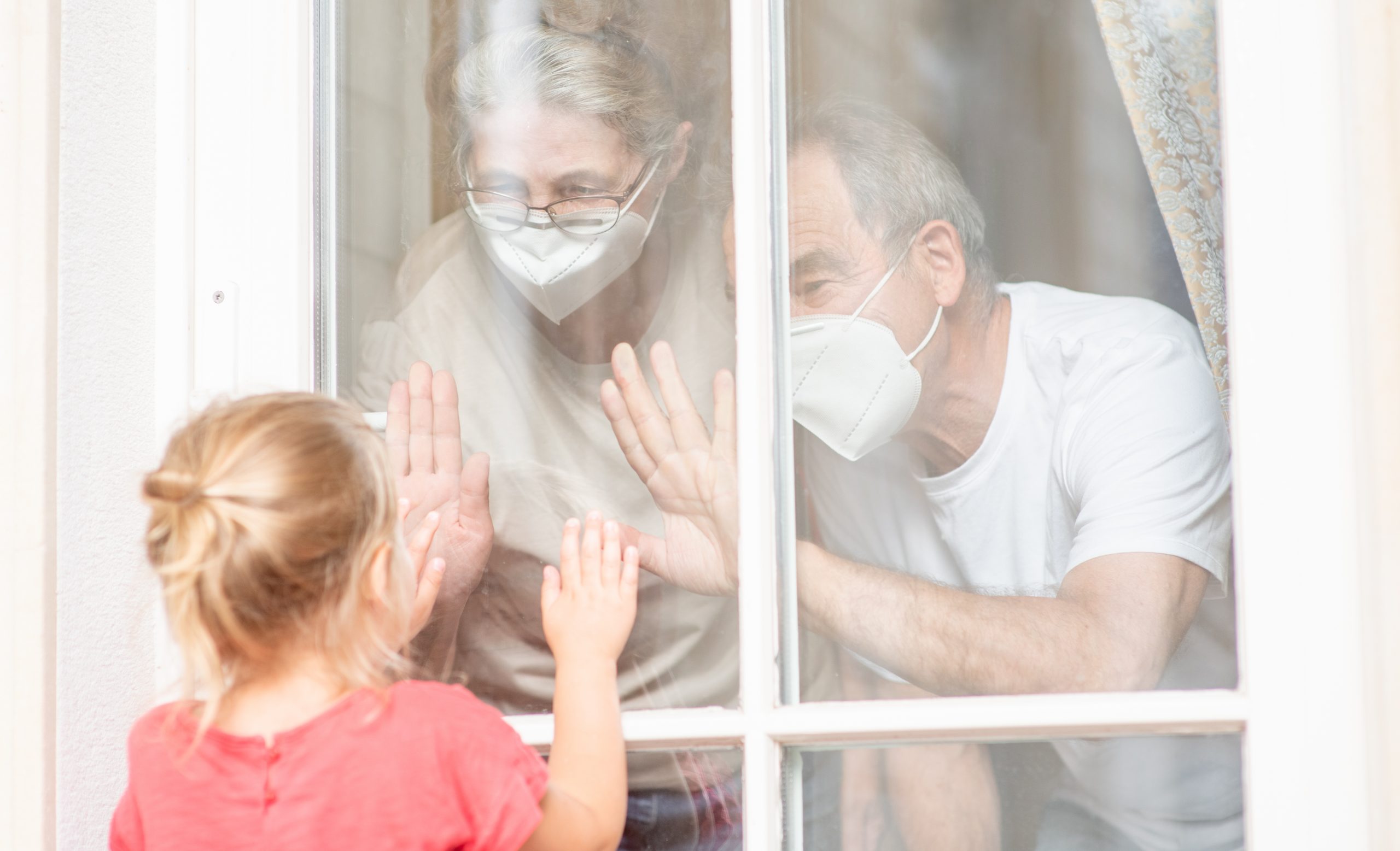 Little girl communicates with his grandparents through a window during the coronavirus epidemic