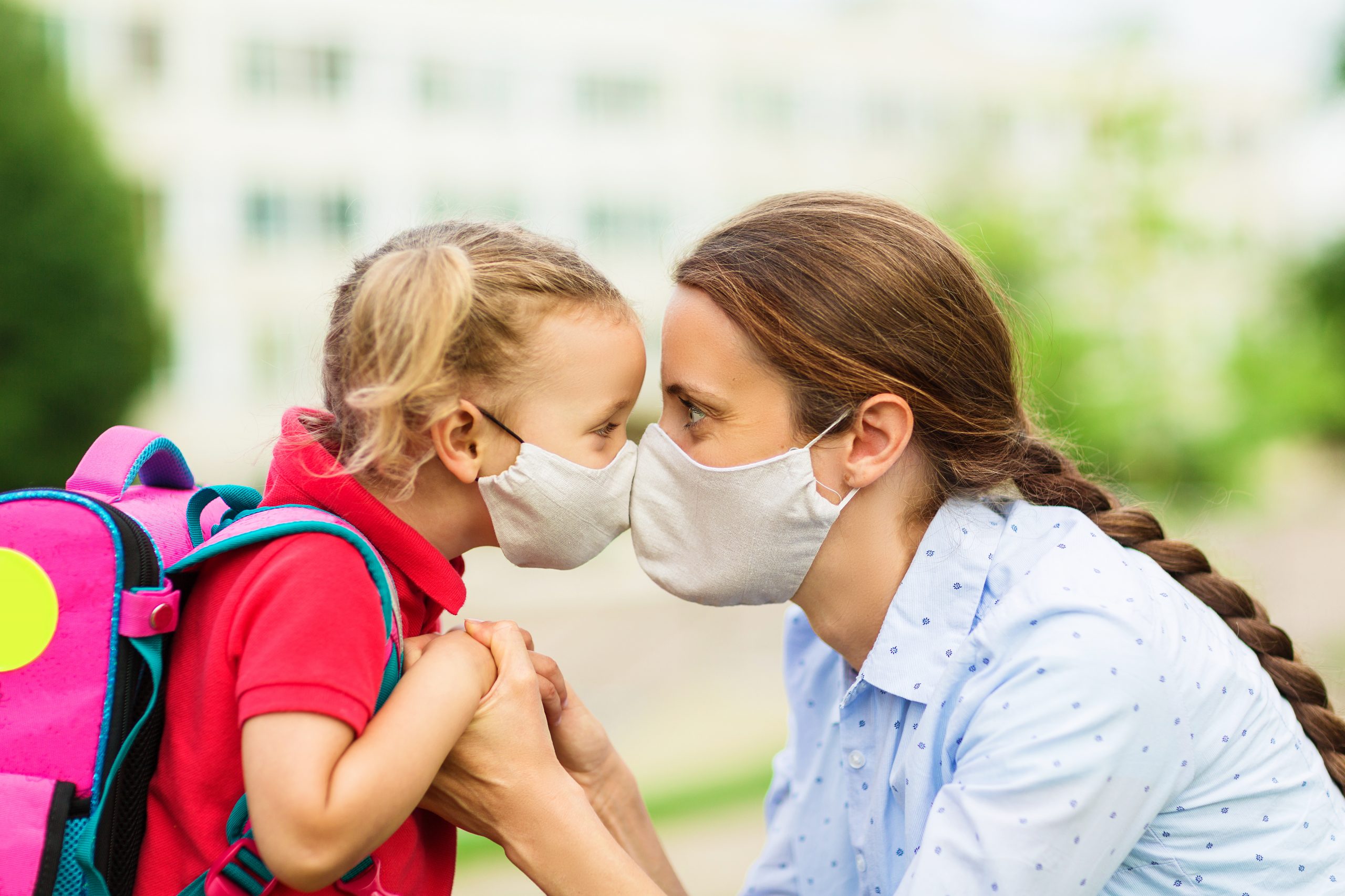 parent and child look into each other's eyes before parting at school and both wear protective medical masks on their faces Close Up