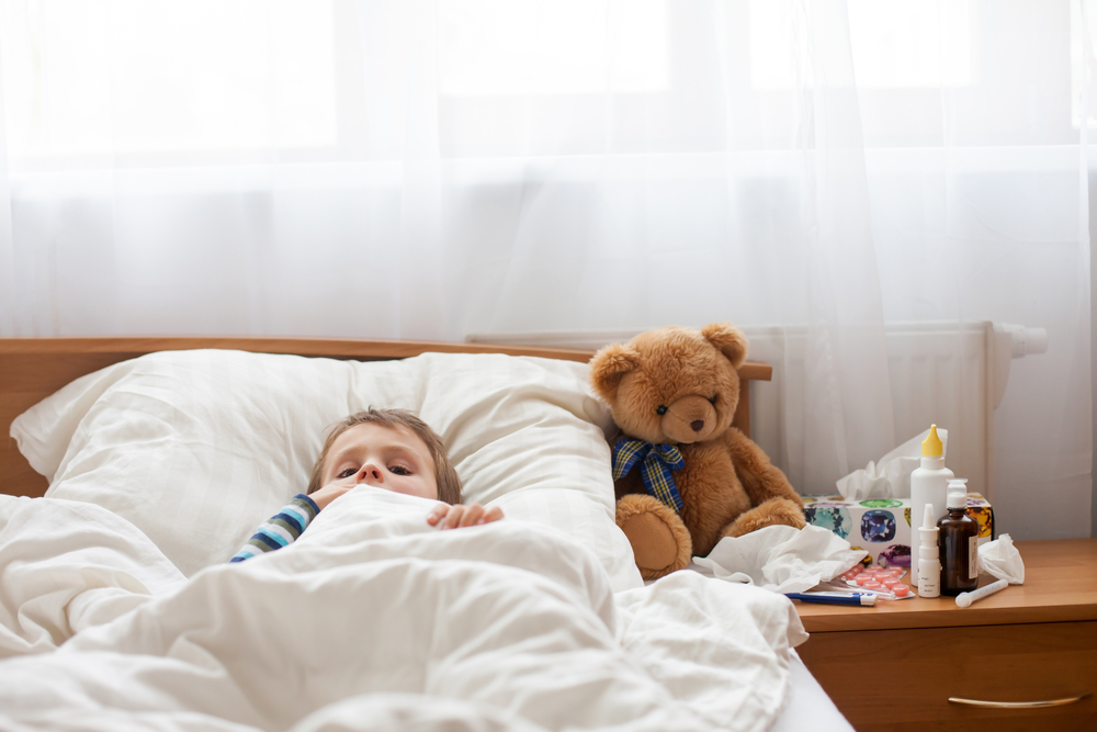 child sick with flu laying in bed with his teddy bear