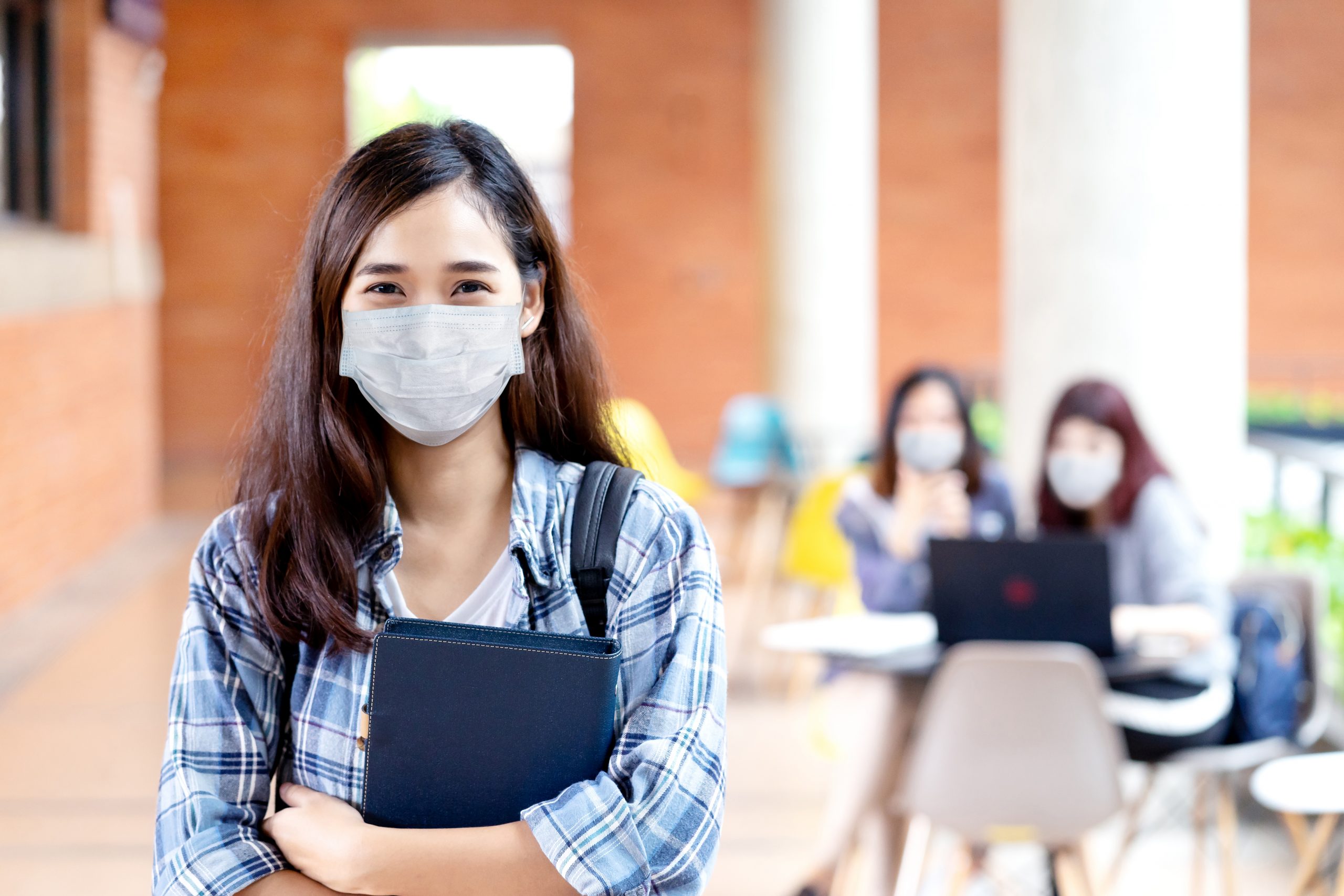 Teenage girl holding folder while wearing a mask and looking at the camera.