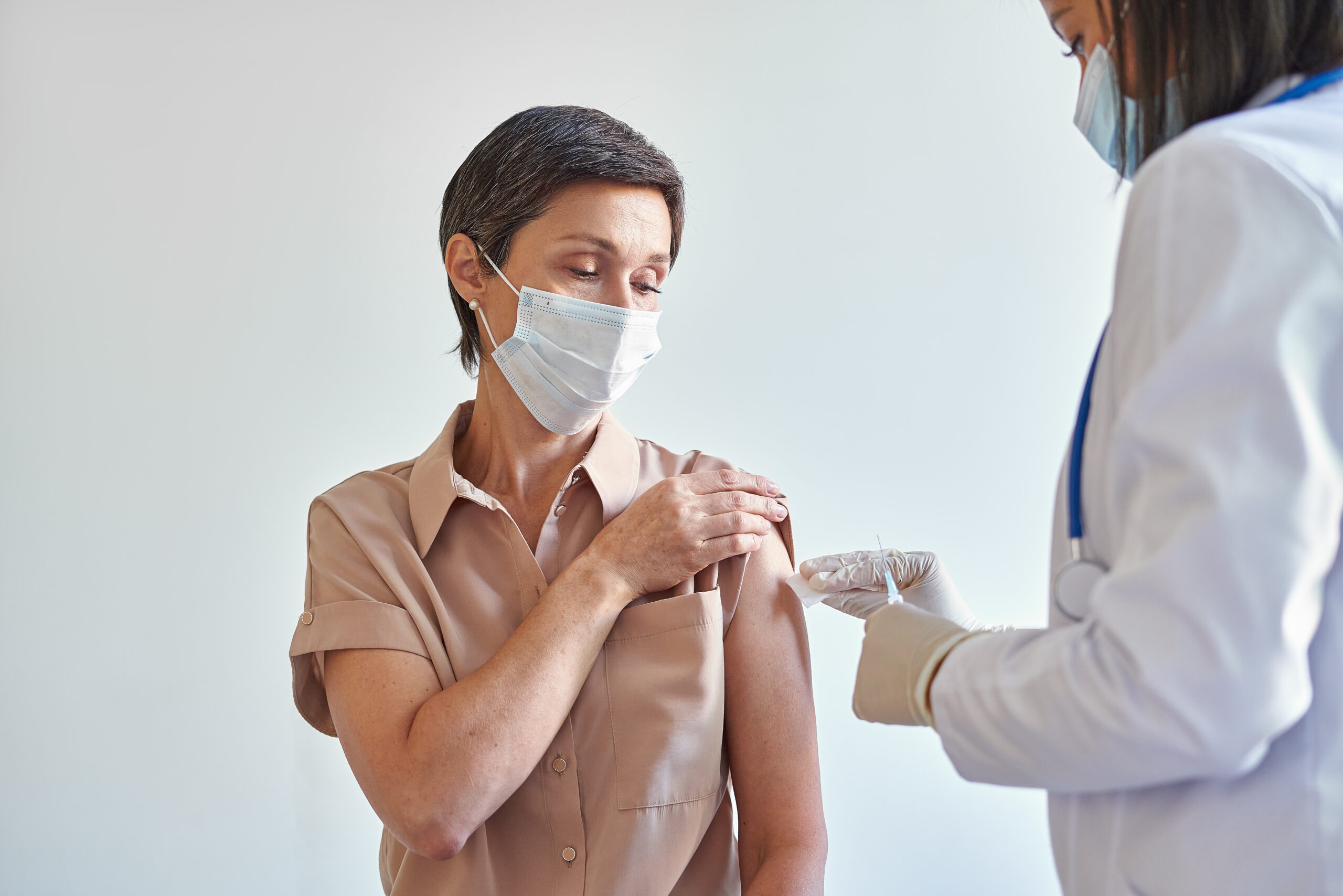 Middle aged woman wearing a mask receives a vaccine in her arm