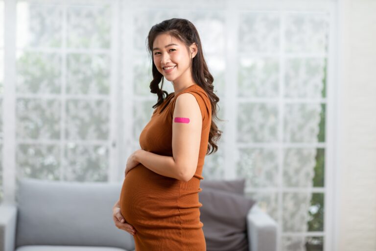 Asian pregnant woman in orange dress. Holding her stomach with a bandage on her arm