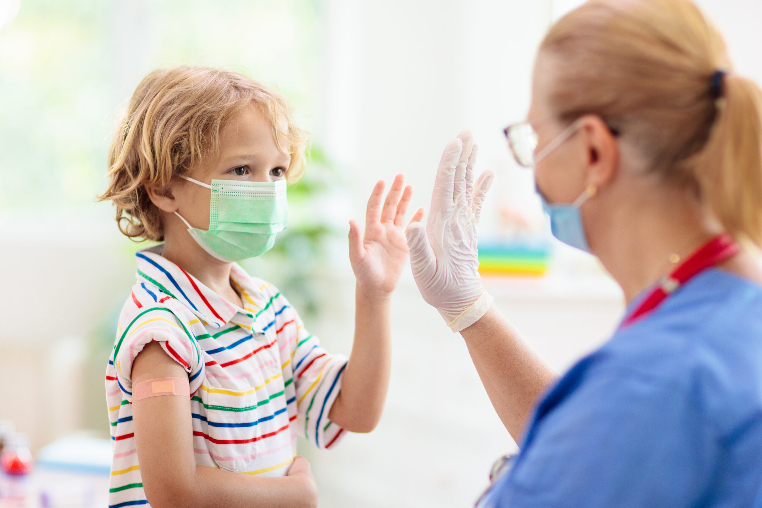 Young child with a mask on gives nurse a high five after receiving vaccine.