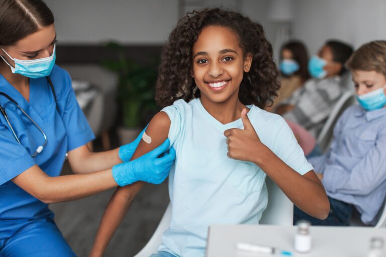 Vaccinated young girl smiling as a healthcare worker puts a bandaid on her arm