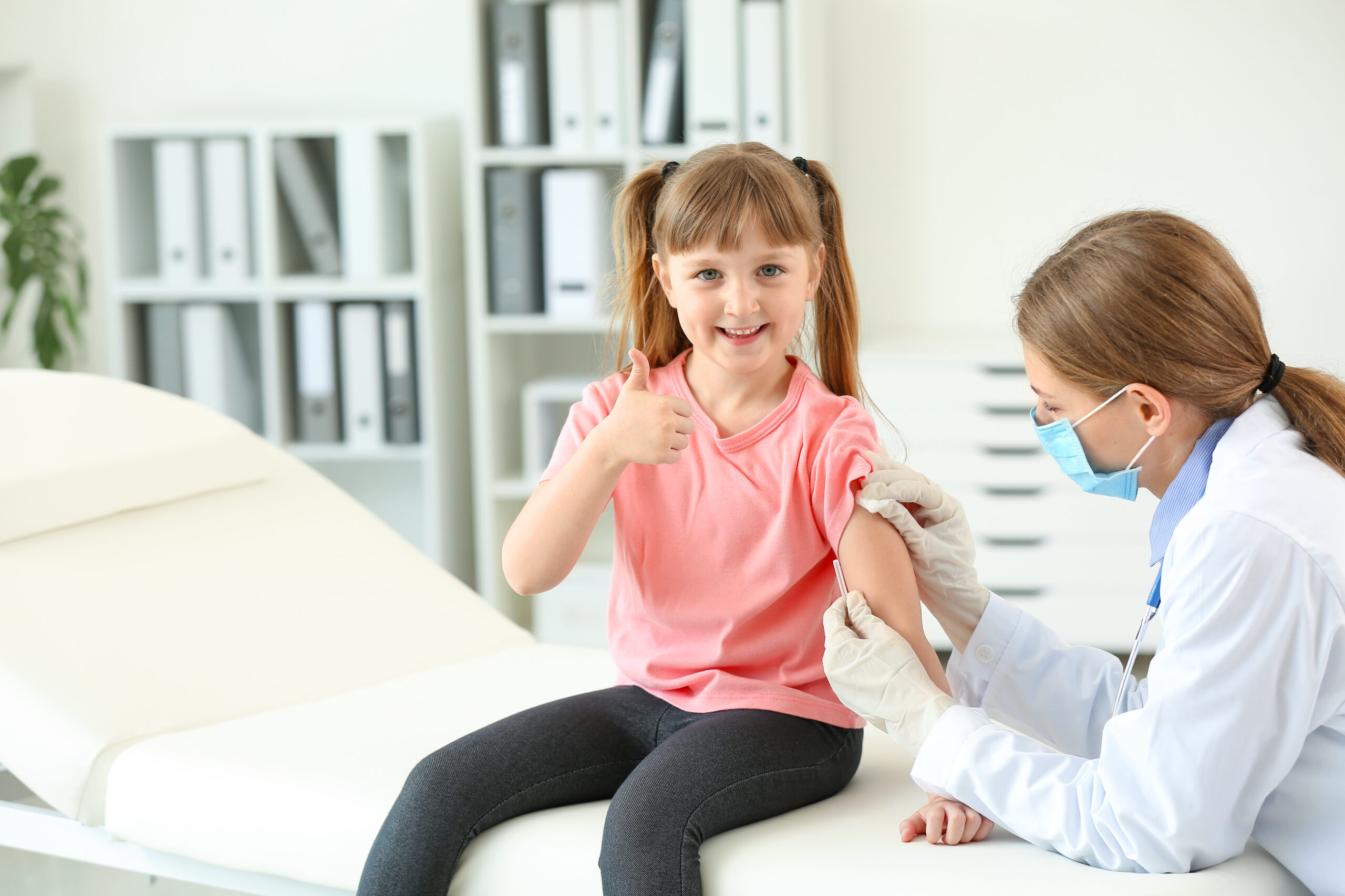 Little girl smiling getting a bandaid put on her arm by a doctor