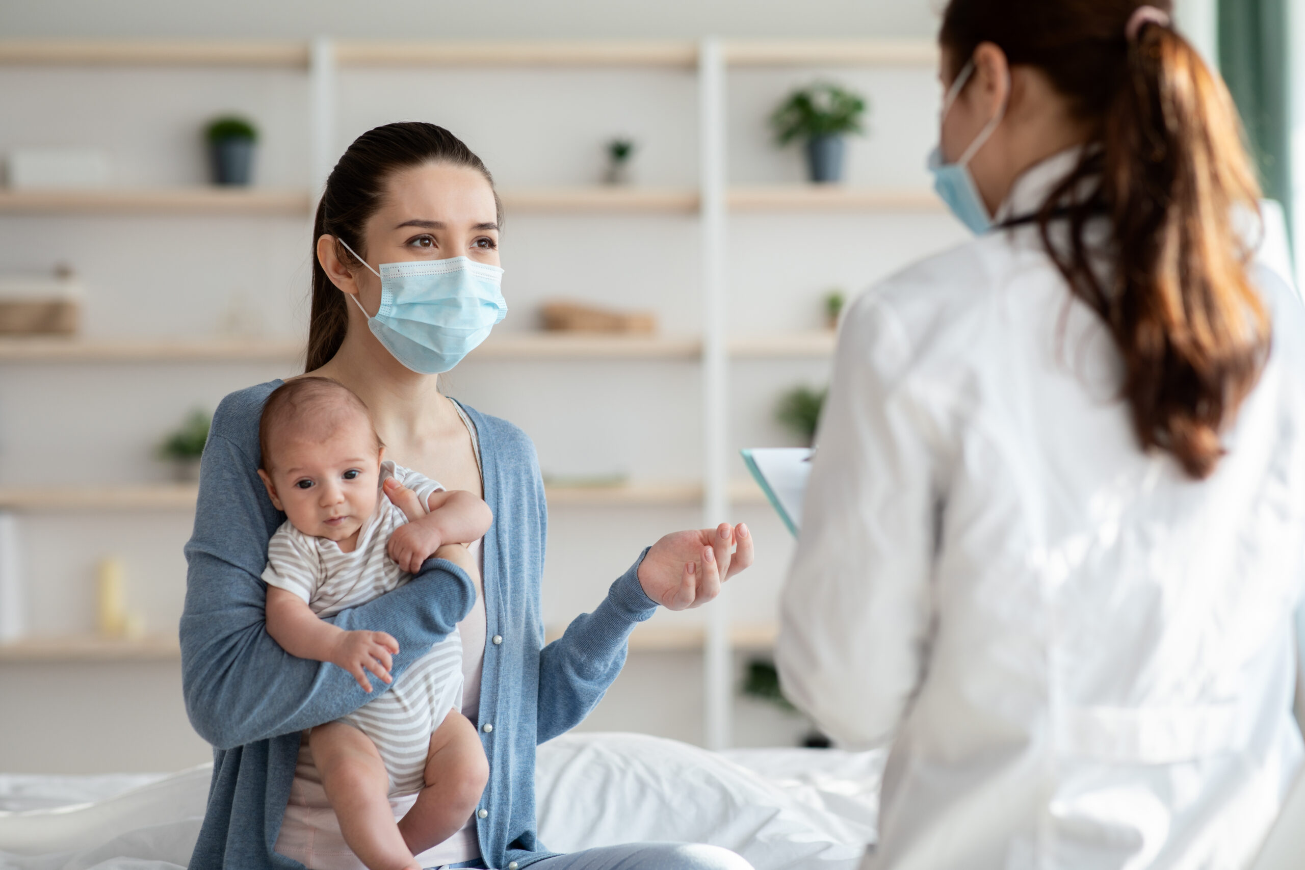 Woman holding her baby at the doctor with a mask