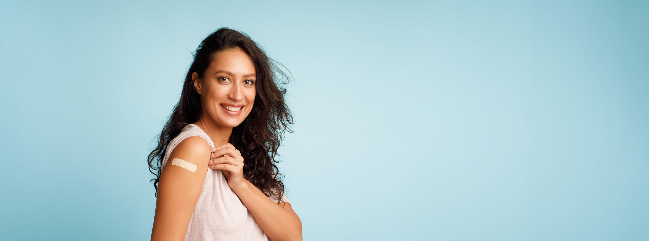 Woman smiling and showing off bandage after getting a vaccine