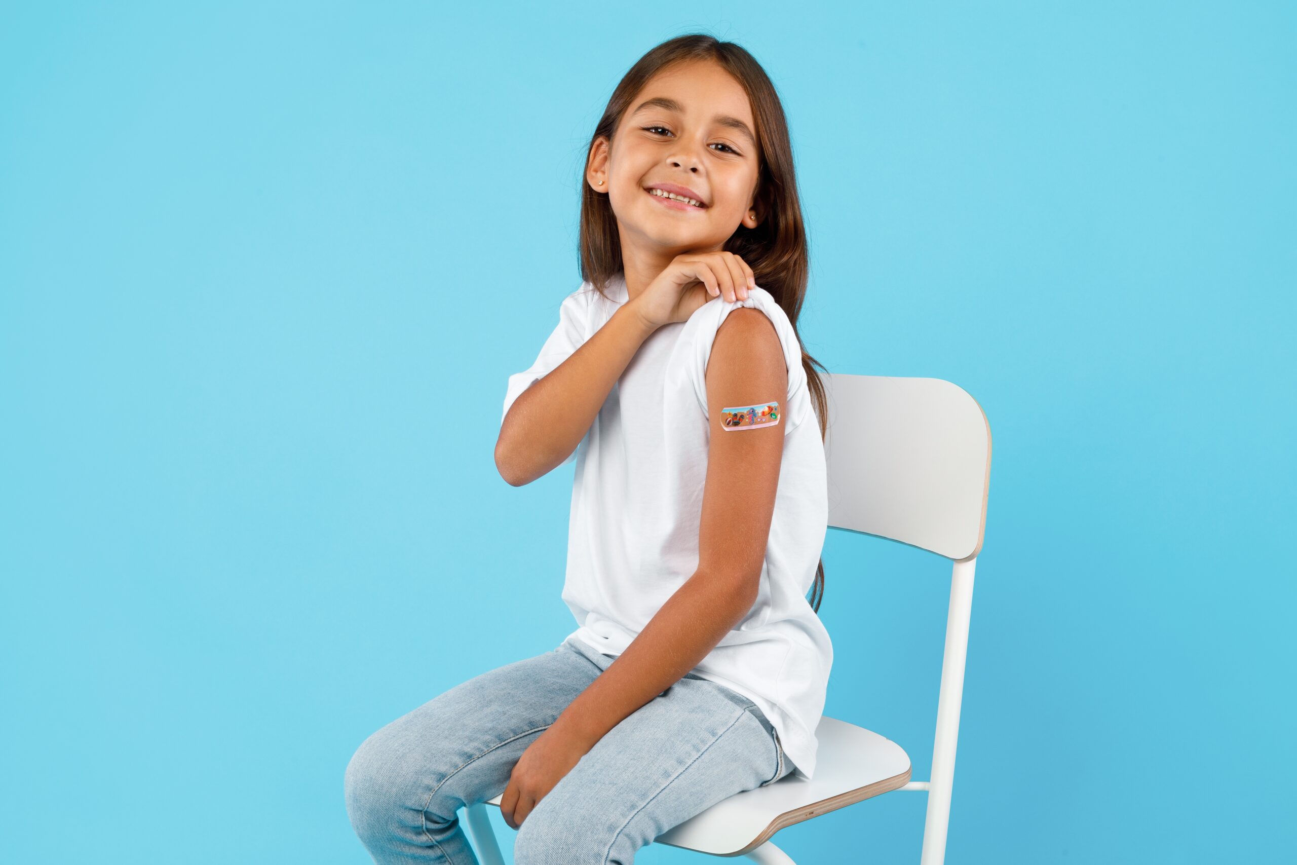 Young girl in chair showing her bandage after getting a vaccine