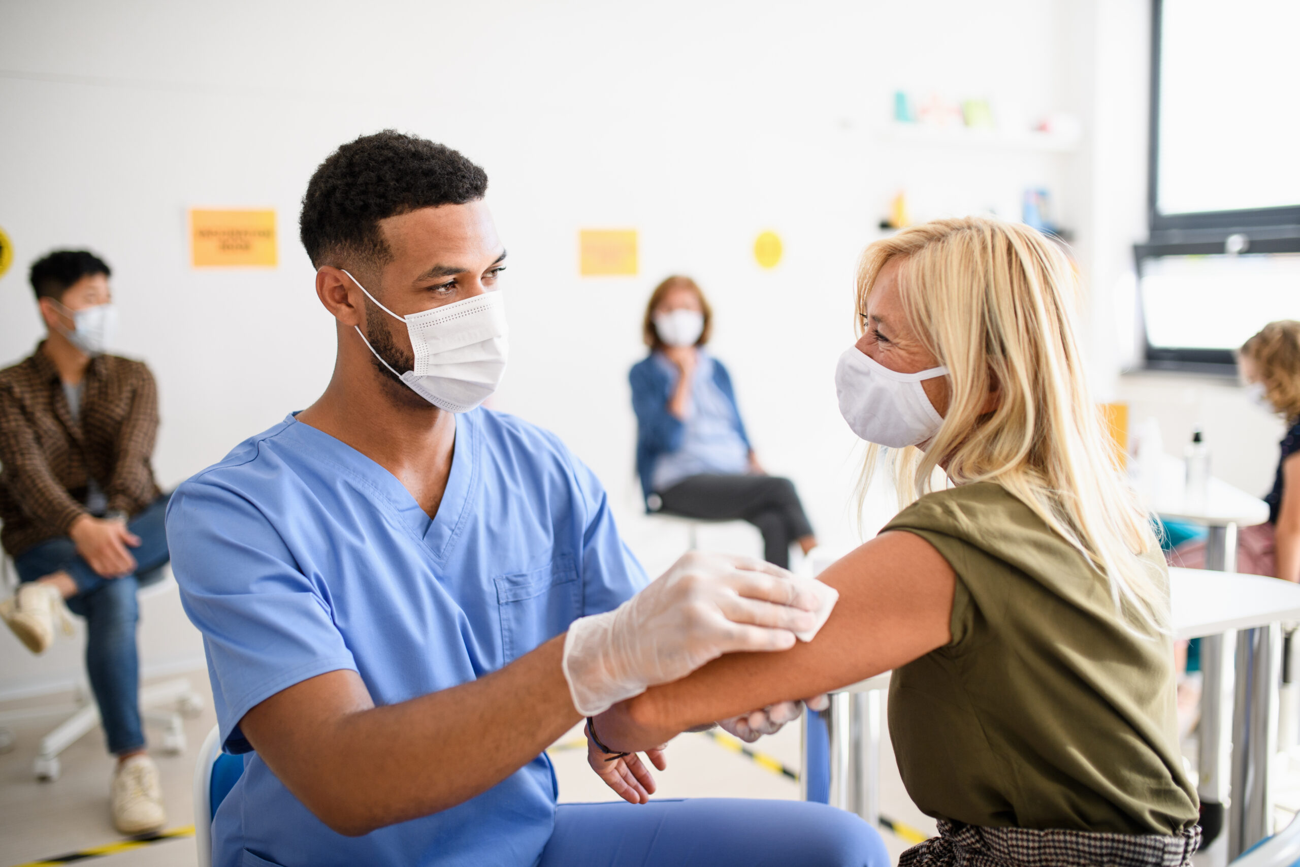 Woman getting a vaccine by a male nurse. Both wearing masks