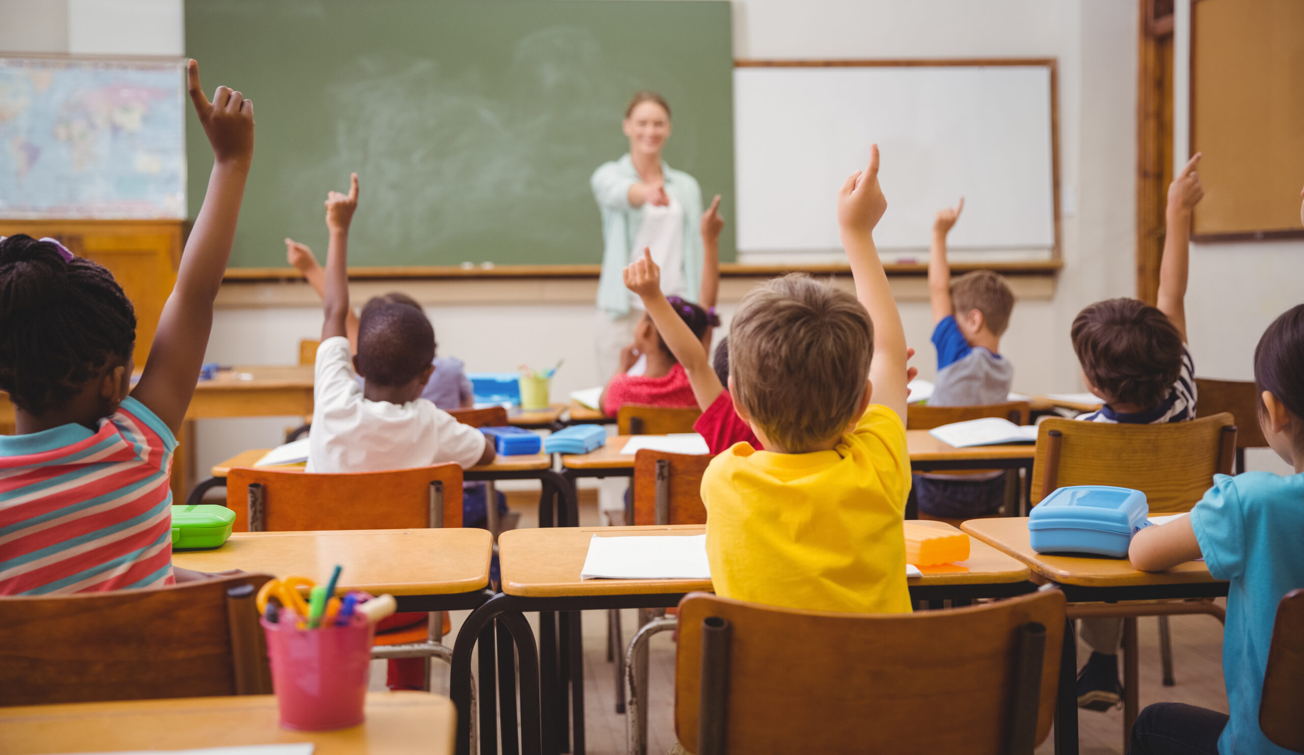 Children in the classroom raising their hands