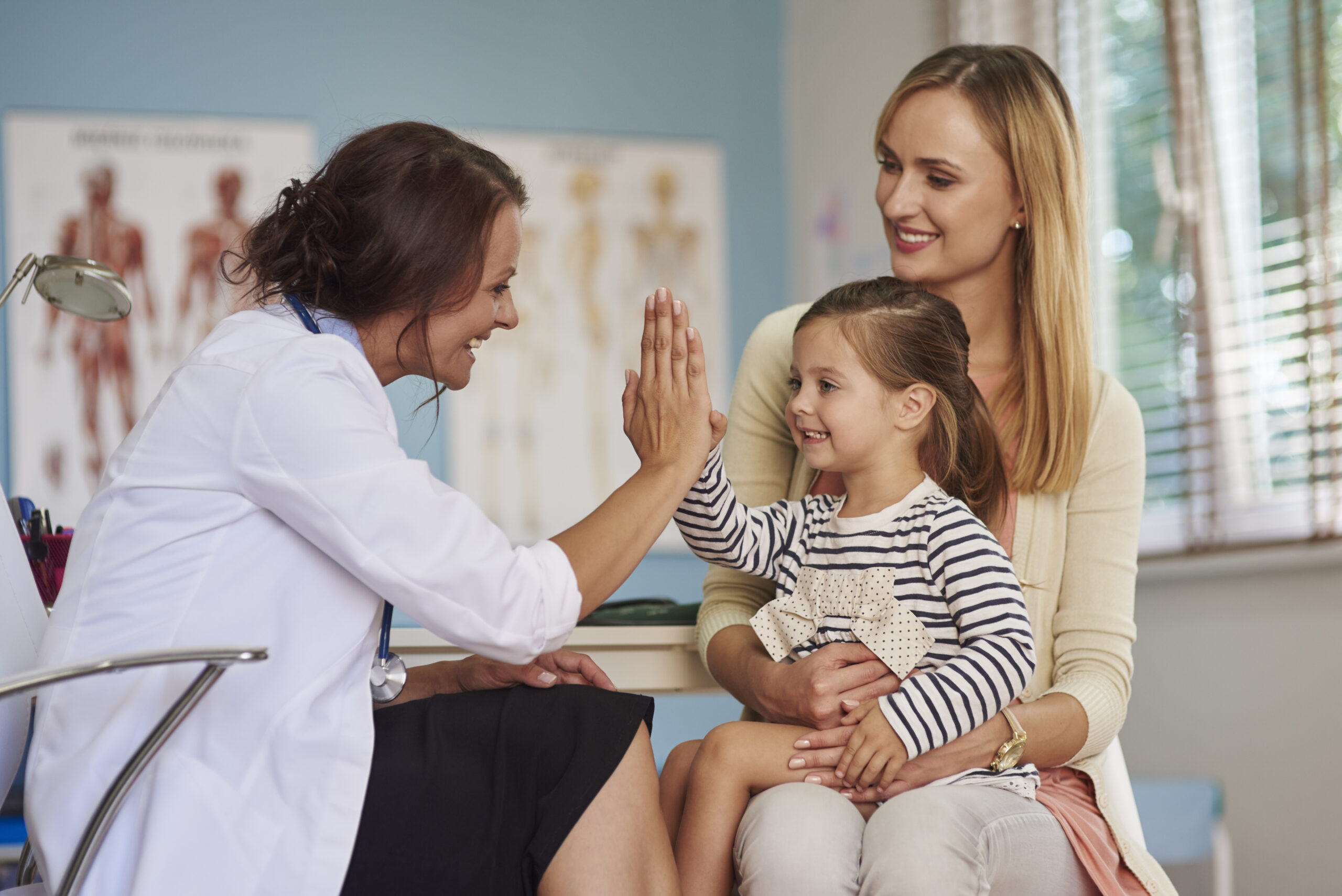 Little girl at the doctor with her mom, giving the doctor a high five