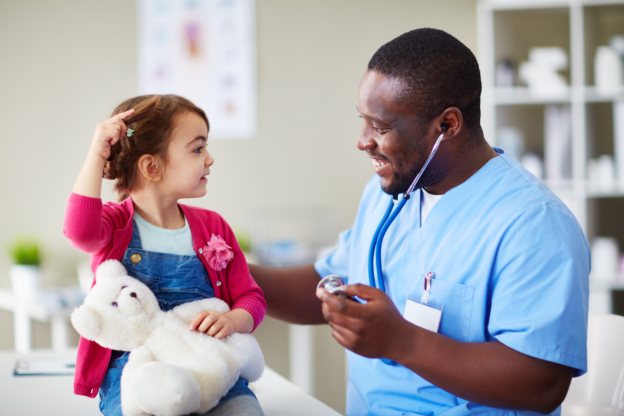 Young girl with teddy bear is talking to her doctor