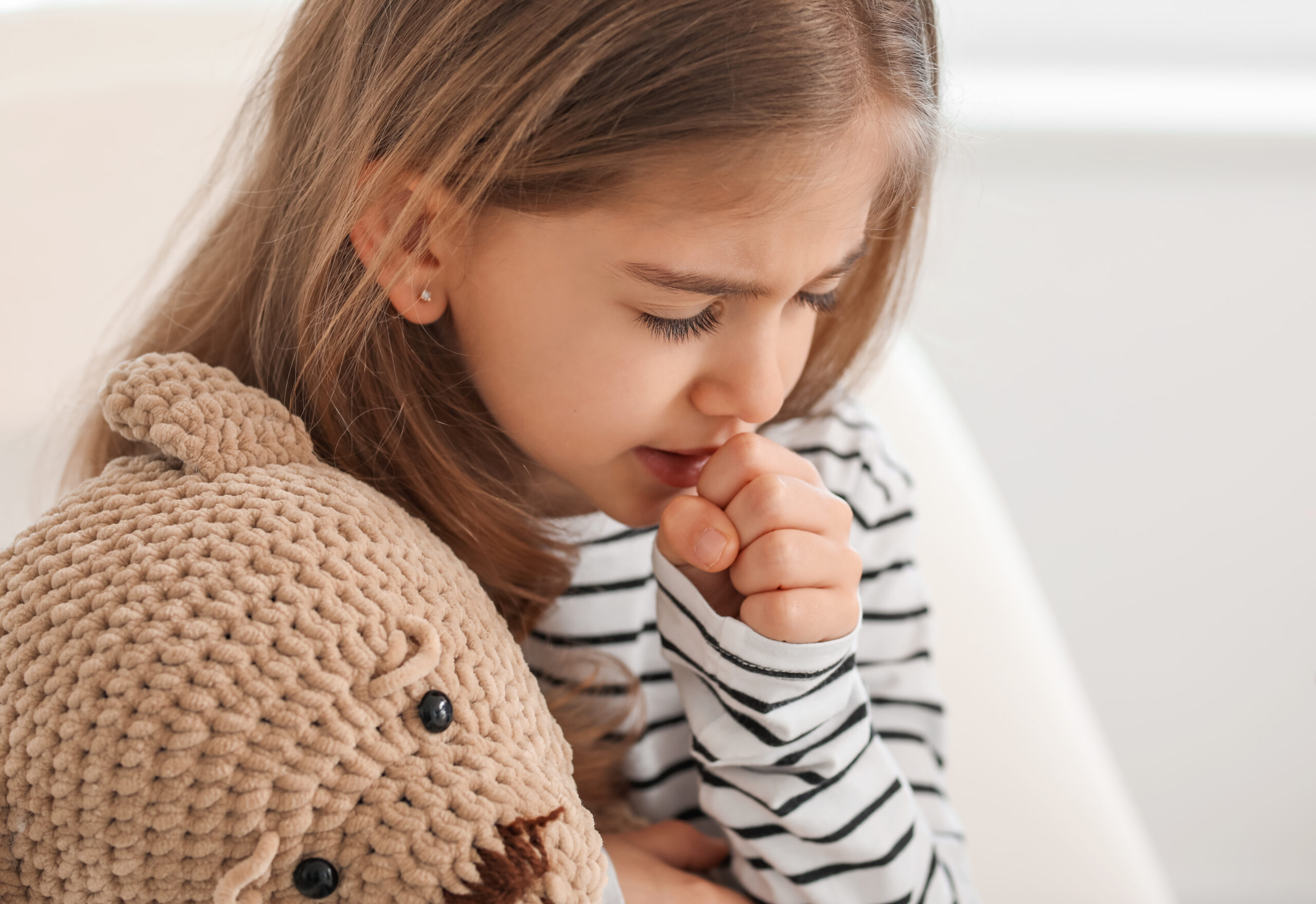 Little girl coughing into her fist while holding her stuffed animal