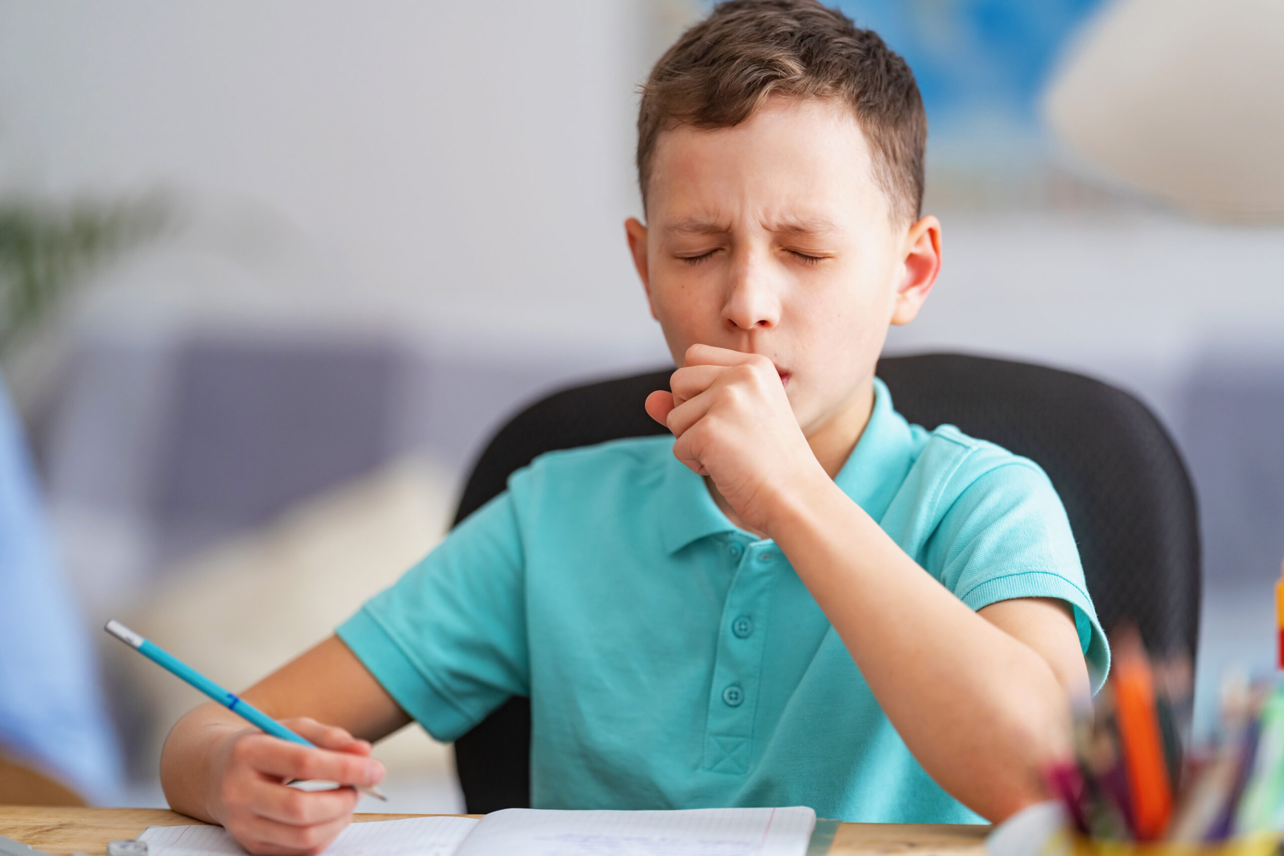 Boy at school coughing as he writes