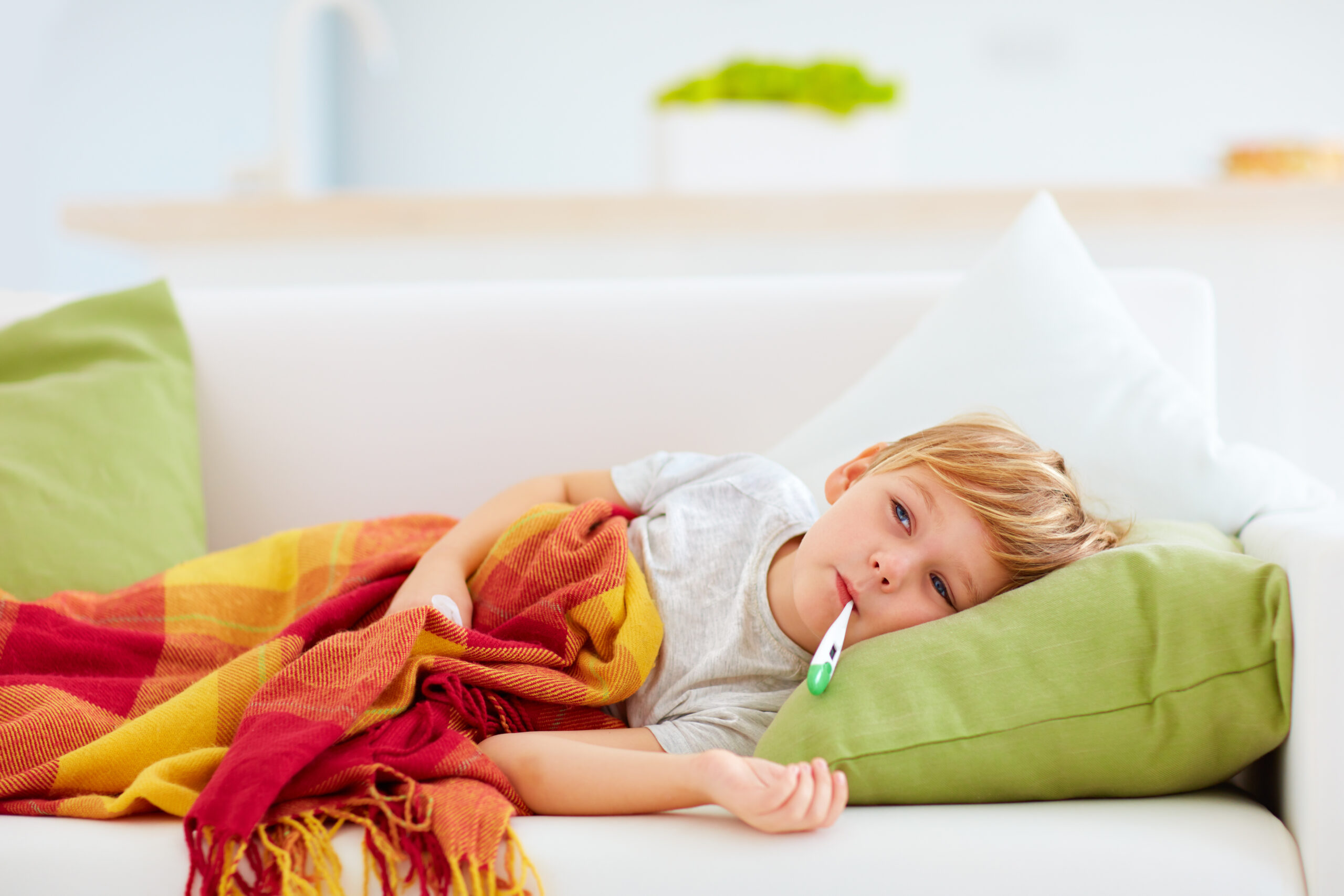 Child laying on a couch with a thermometer in his mouth